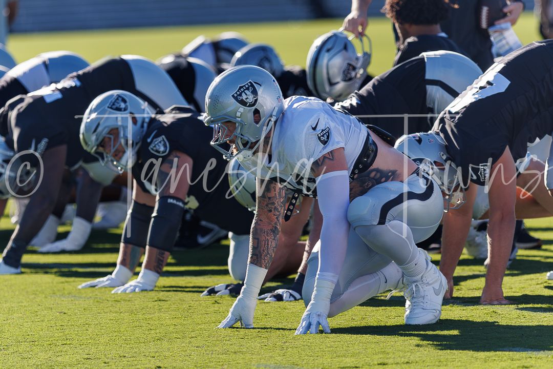 NFL Raiders players line up at scrimmage during a sunny outdoor practice session on a green field.