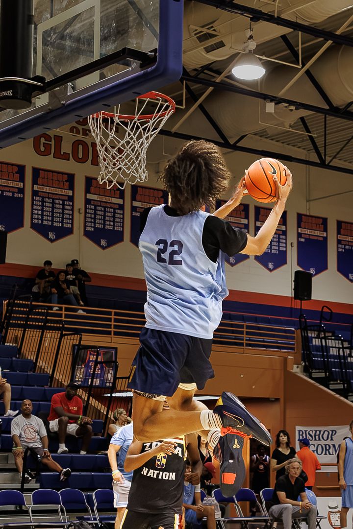 Player #22 leaps toward the basketball hoop during an indoor game, ball in hand, in a blue jersey.