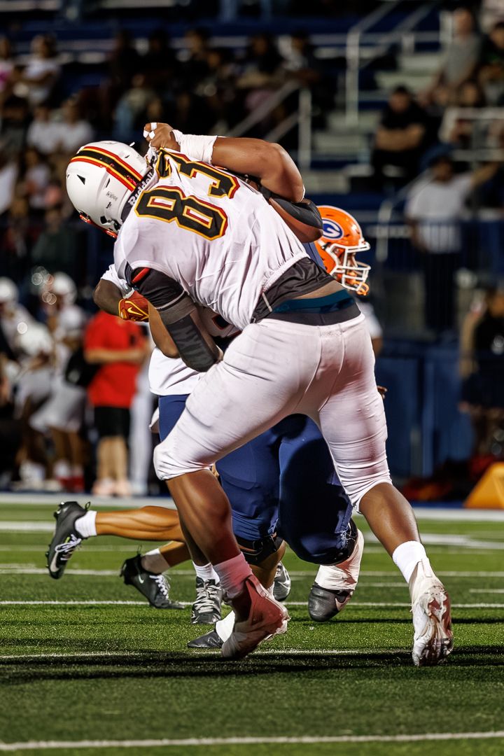 Two football players collide during a night game, one in white jersey #83 tackling a player in blue and orange uniform.
