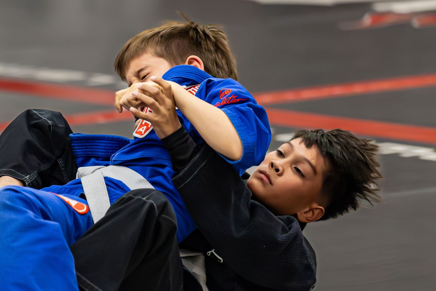 Two children sparring in Brazilian jiu-jitsu gi uniforms on a martial arts mat during kids BJJ training class.