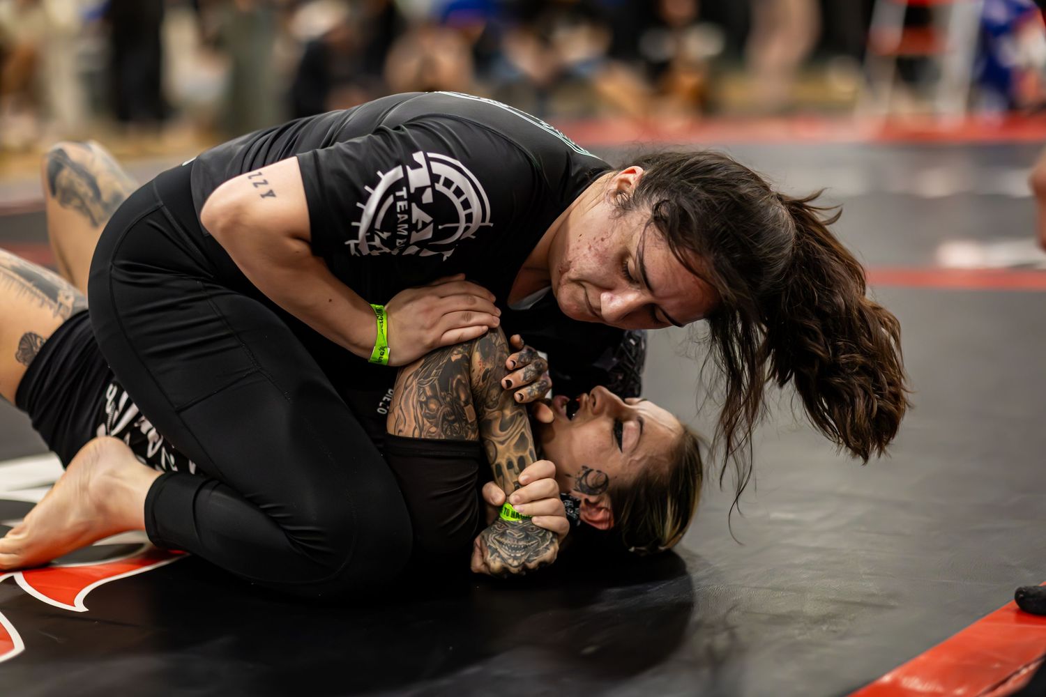 Two competitors grappling on the mat during a Brazilian jiu-jitsu tournament match.