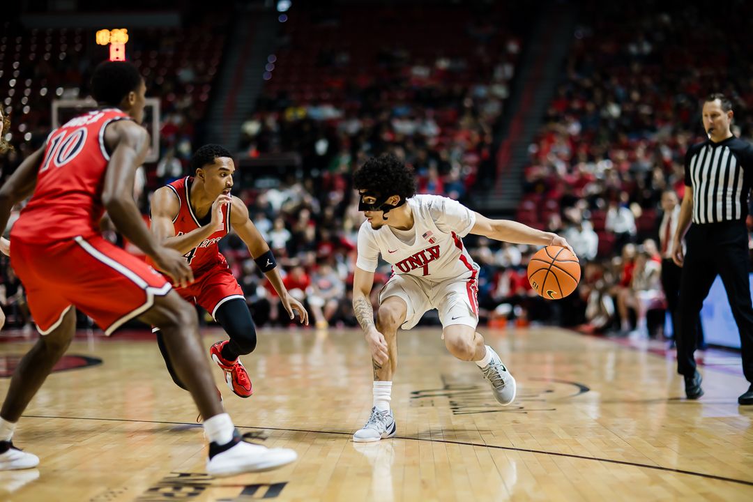 Basketball players dive for a loose ball during an intense college basketball game on the hardwood court.
