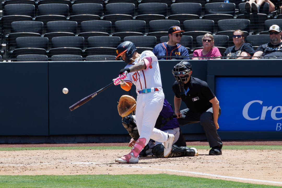 A baseball batter swings at a pitch during a game with an umpire and catcher positioned behind home plate.