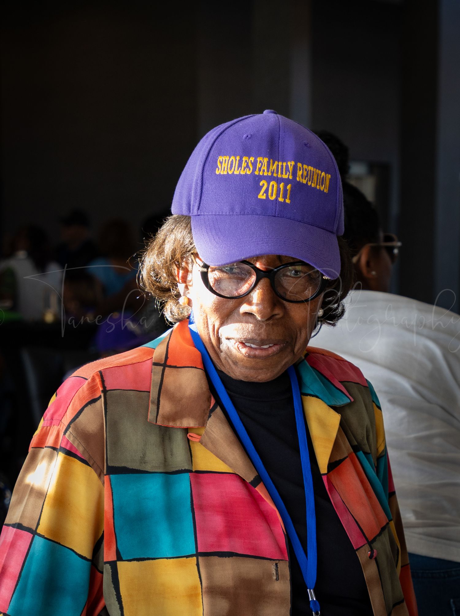 Participant wearing colorful patchwork jacket and purple cap smiles at community event.