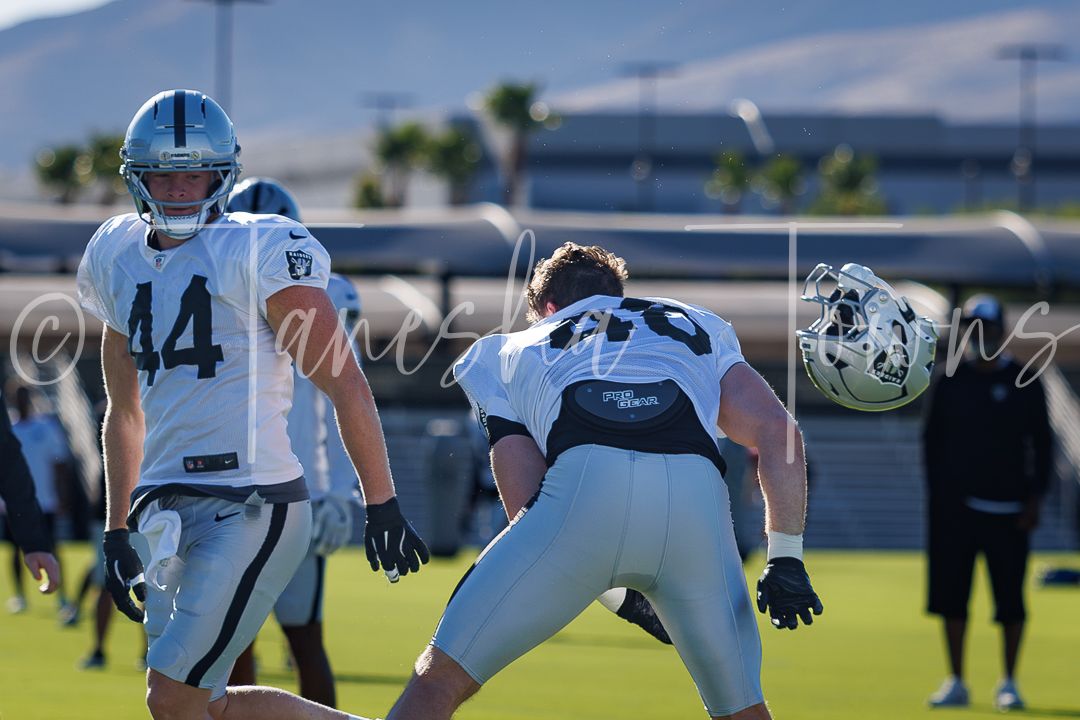 Raiders football players in black and white uniforms practice drills on a green field during an outdoor training session.