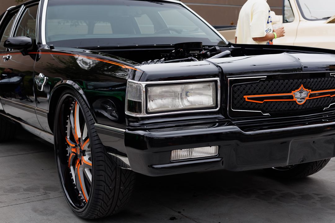 A sleek black classic car with custom orange and black rims parked outdoors.