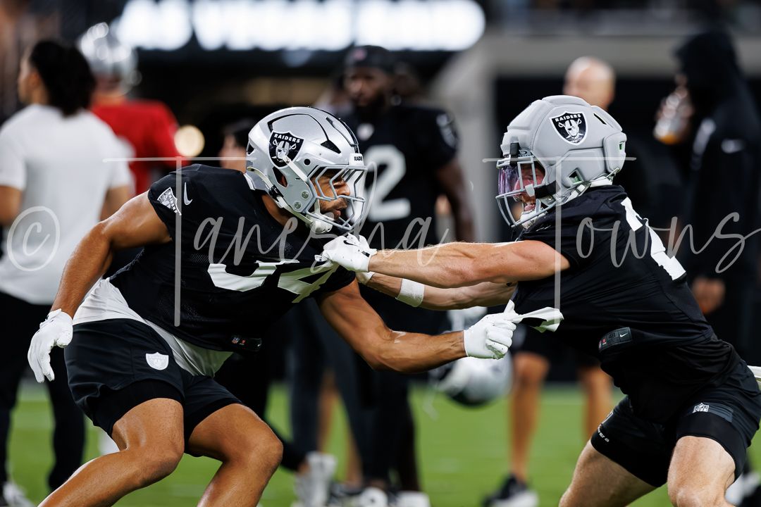 Two Las Vegas Raiders players practice drills in black uniforms at Allegiant Stadium during NFL training camp.