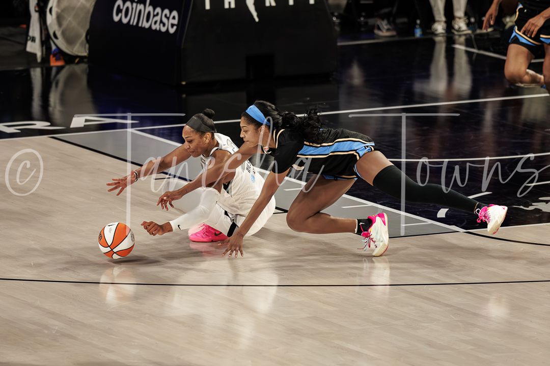 Two WNBA players dive for a loose ball during a competitive game, with Coinbase signage visible in the background.