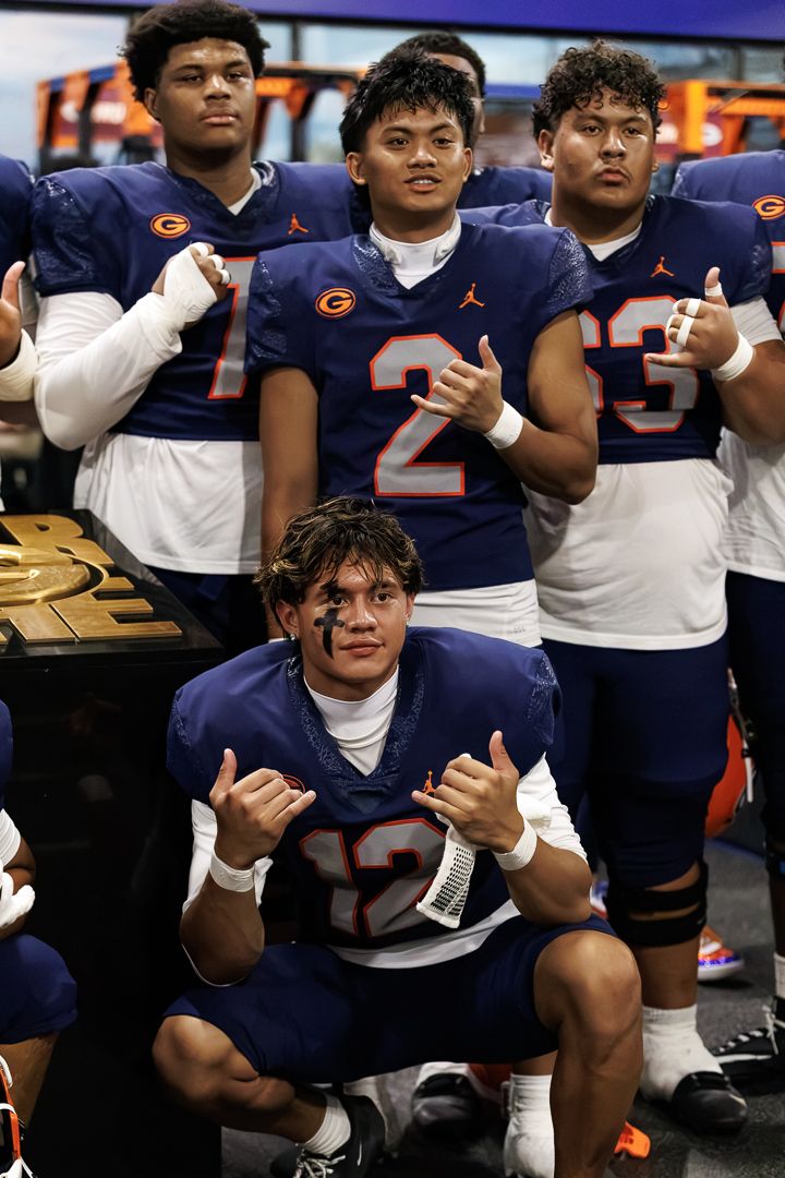 Football players in navy blue Jordan uniforms pose together, flashing hand signs after a victory game.