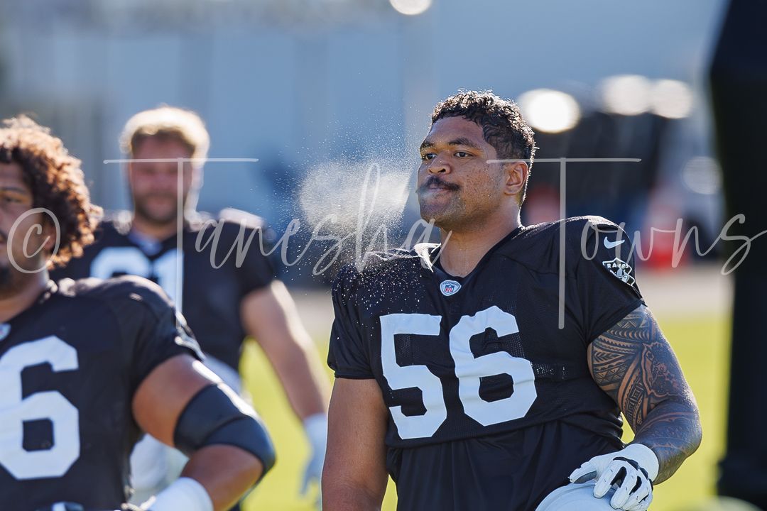 Football player wearing jersey number 56 in dark uniform smiling during outdoor practice session.