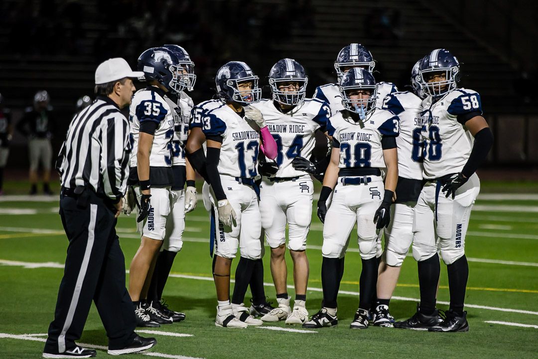 Football teams gather on field with officials during a nighttime game.