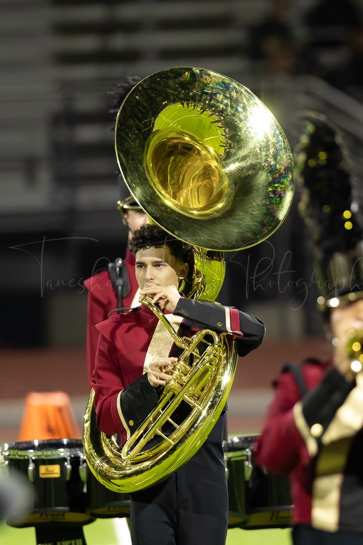 Sousaphone player performing with marching band under stadium lights.