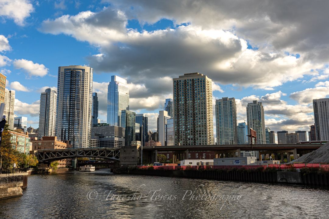 Modern glass skyscrapers line the waterfront of a city skyline under dramatic cloudy skies.
