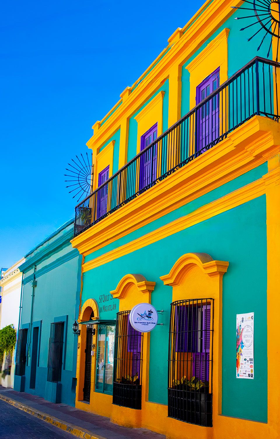 Colorful colonial buildings with yellow and turquoise facades featuring ornate balconies along a street.
