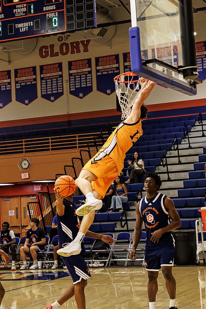 Player in orange jersey dunks basketball in indoor gym with Glory signage and blue bleachers.