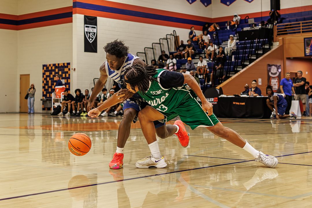 Two basketball players battle for a loose ball on an indoor court during a competitive high school game.