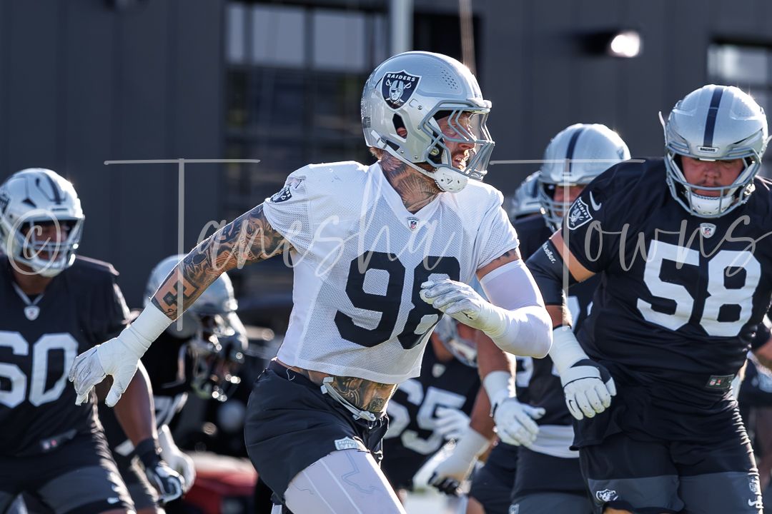Raiders player #98 in white uniform running drills during NFL team practice.