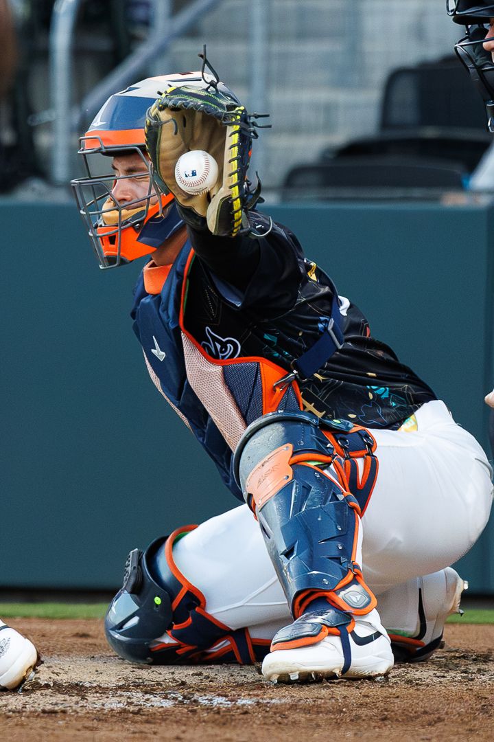 Baseball catcher in orange and navy uniform prepares to catch a pitch.