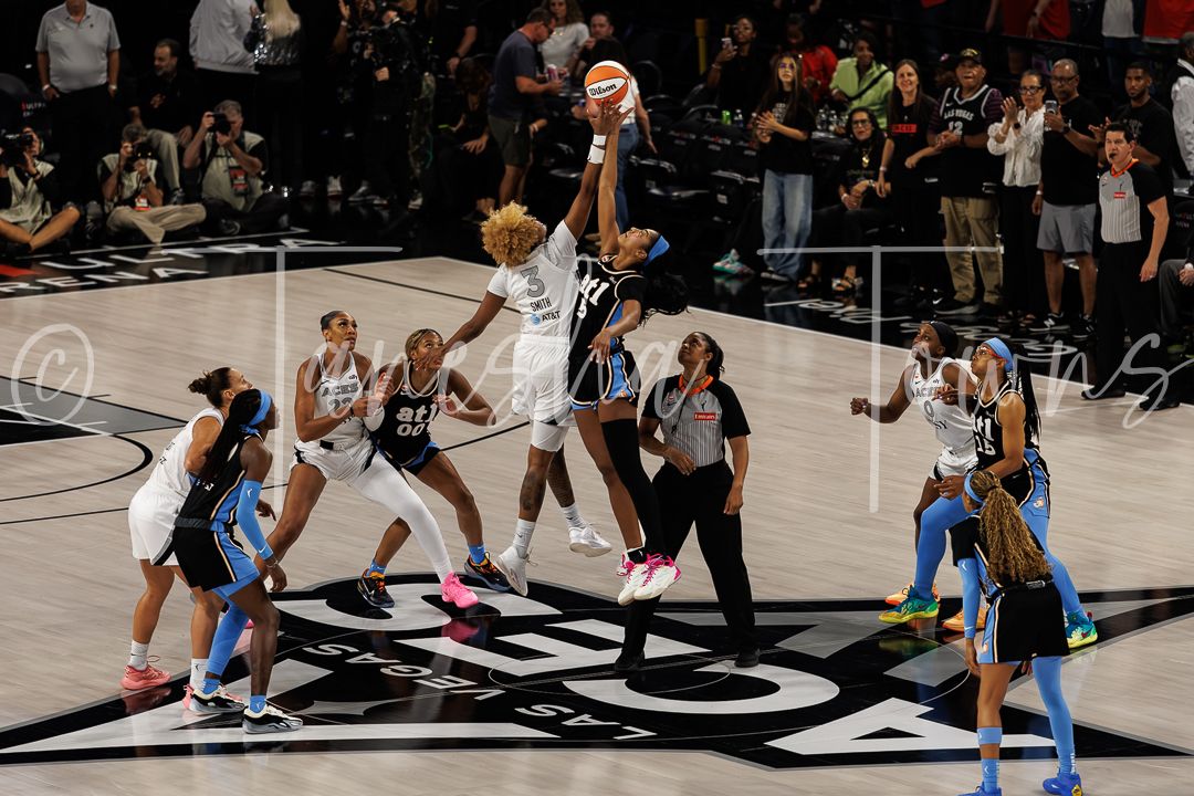 WNBA players jump for tip-off at center court during a competitive women's basketball game.