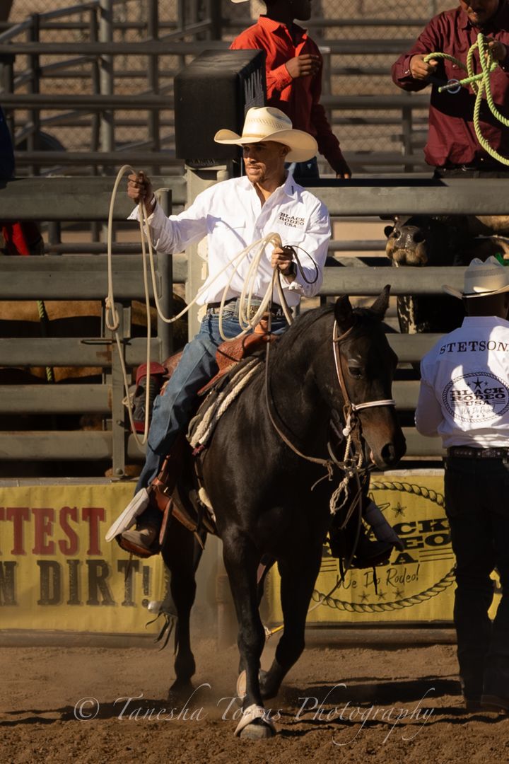 A rider in a white shirt and cowboy hat sits atop a black horse during a western rodeo competition.