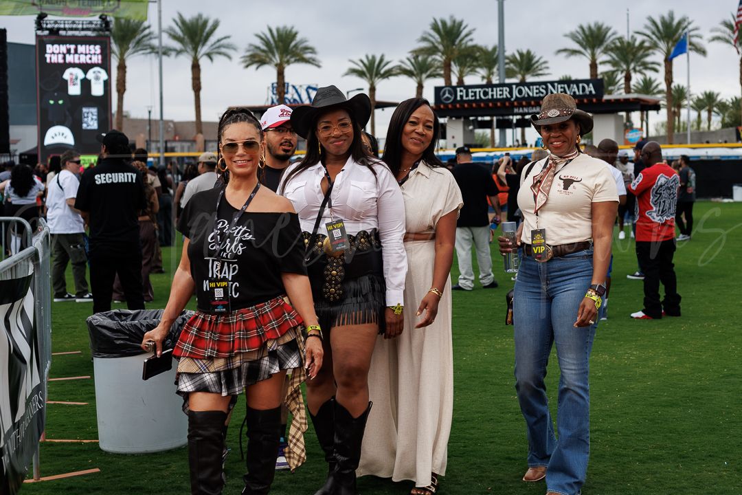 Group of women posing in country western outfits at outdoor music festival.