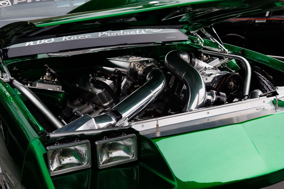 Green custom car with open hood showcasing a chrome-piped high-performance engine bay.