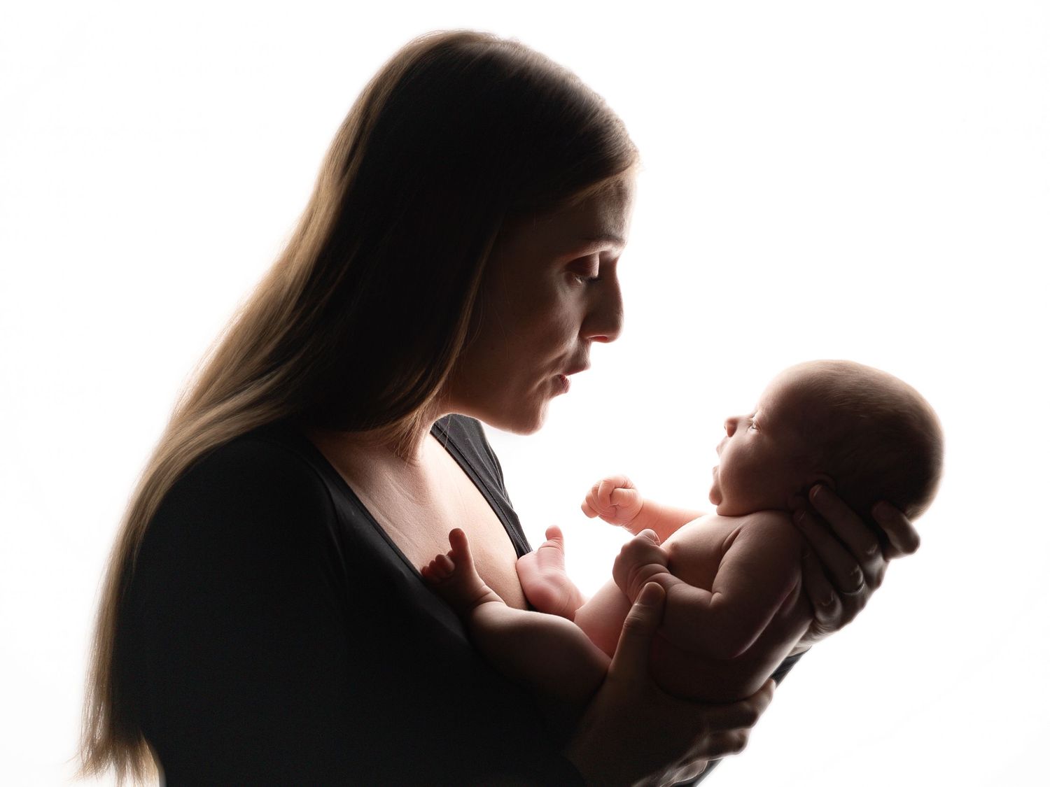 Silhouetted profile of mother holding newborn baby against white background.