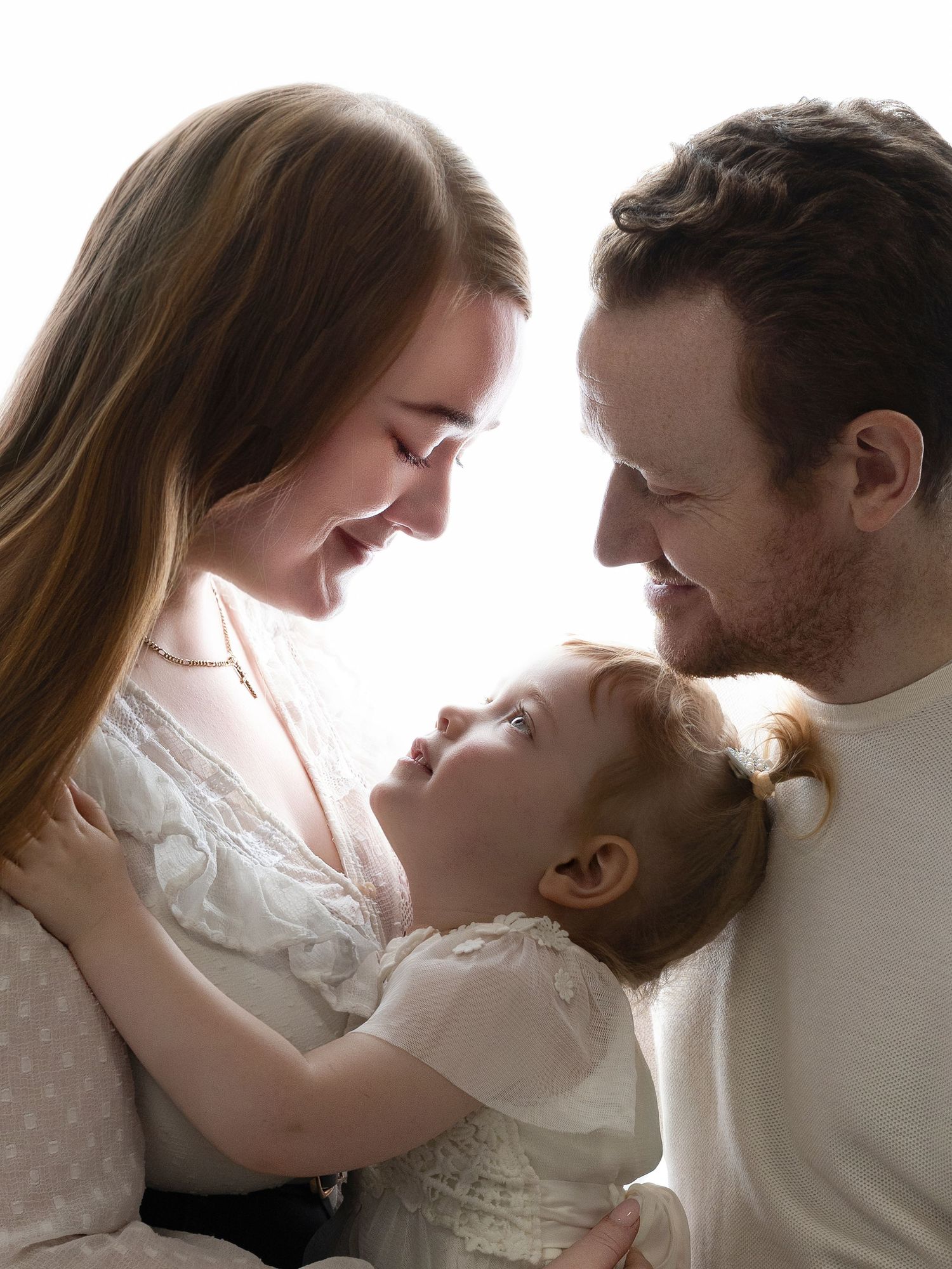 A loving family portrait of a mother, father, and young toddler girl sharing a tender moment together.