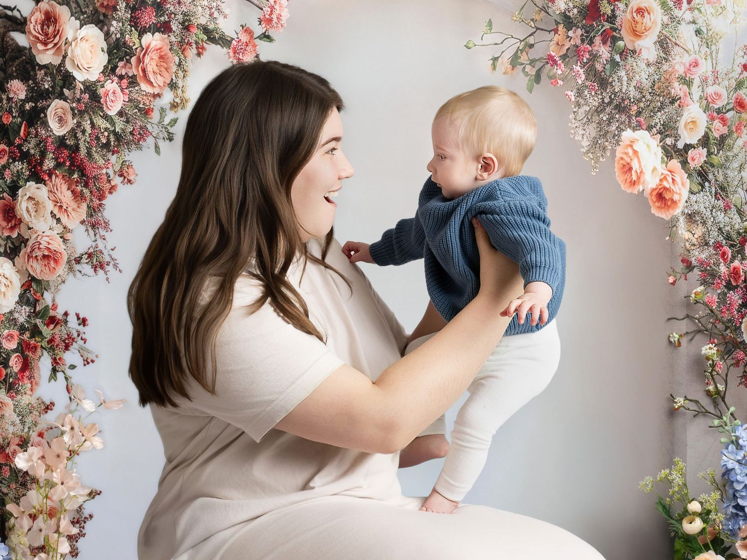 A parent and baby share joyful moments against a floral backdrop in a professional photography studio.