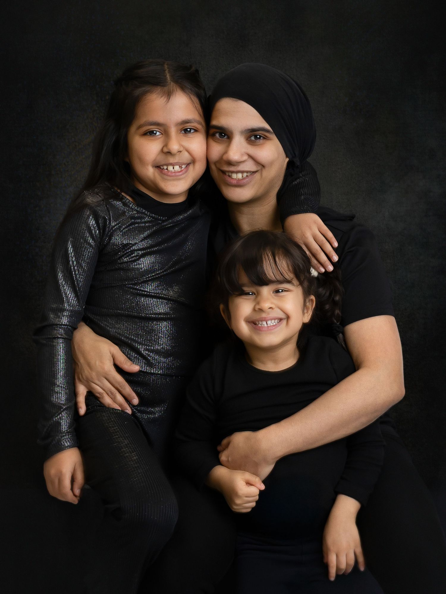 A heartwarming family portrait against a dark background showing warm smiles and matching black outfits.