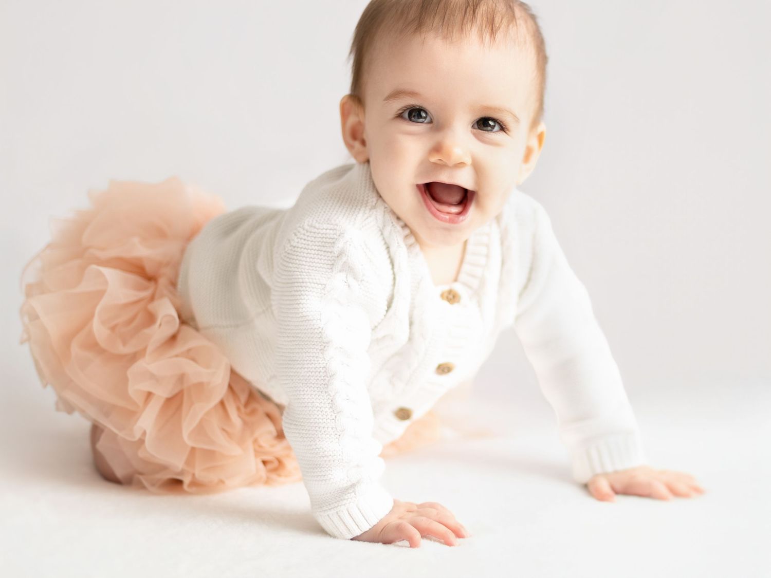 A baby wearing a white outfit and peach tutu lies on a light background in a series of playful poses.