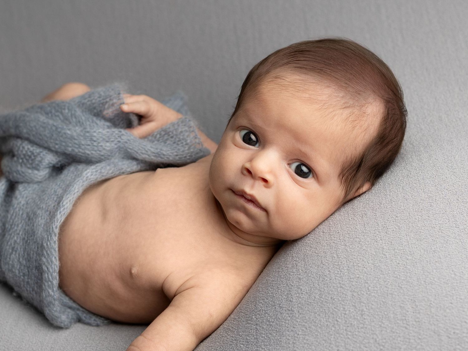 Baby wearing grey knit accessory lying on soft grey background.