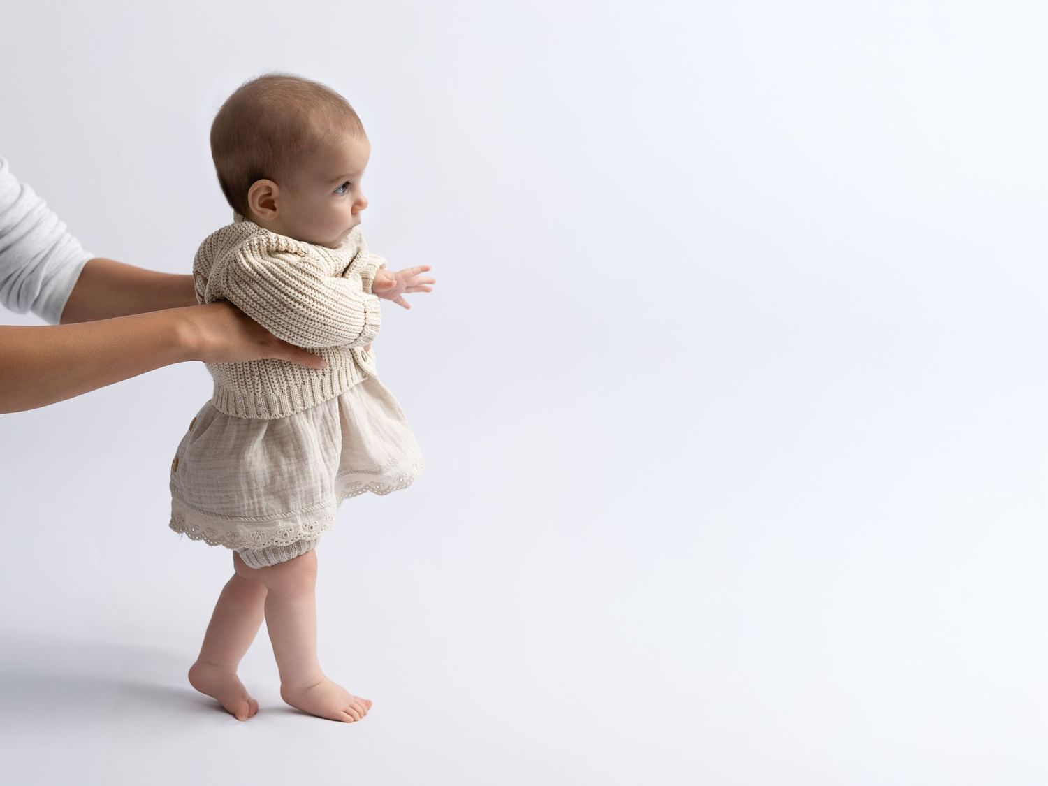 Baby in cream colored outfit showing standing and sitting poses.