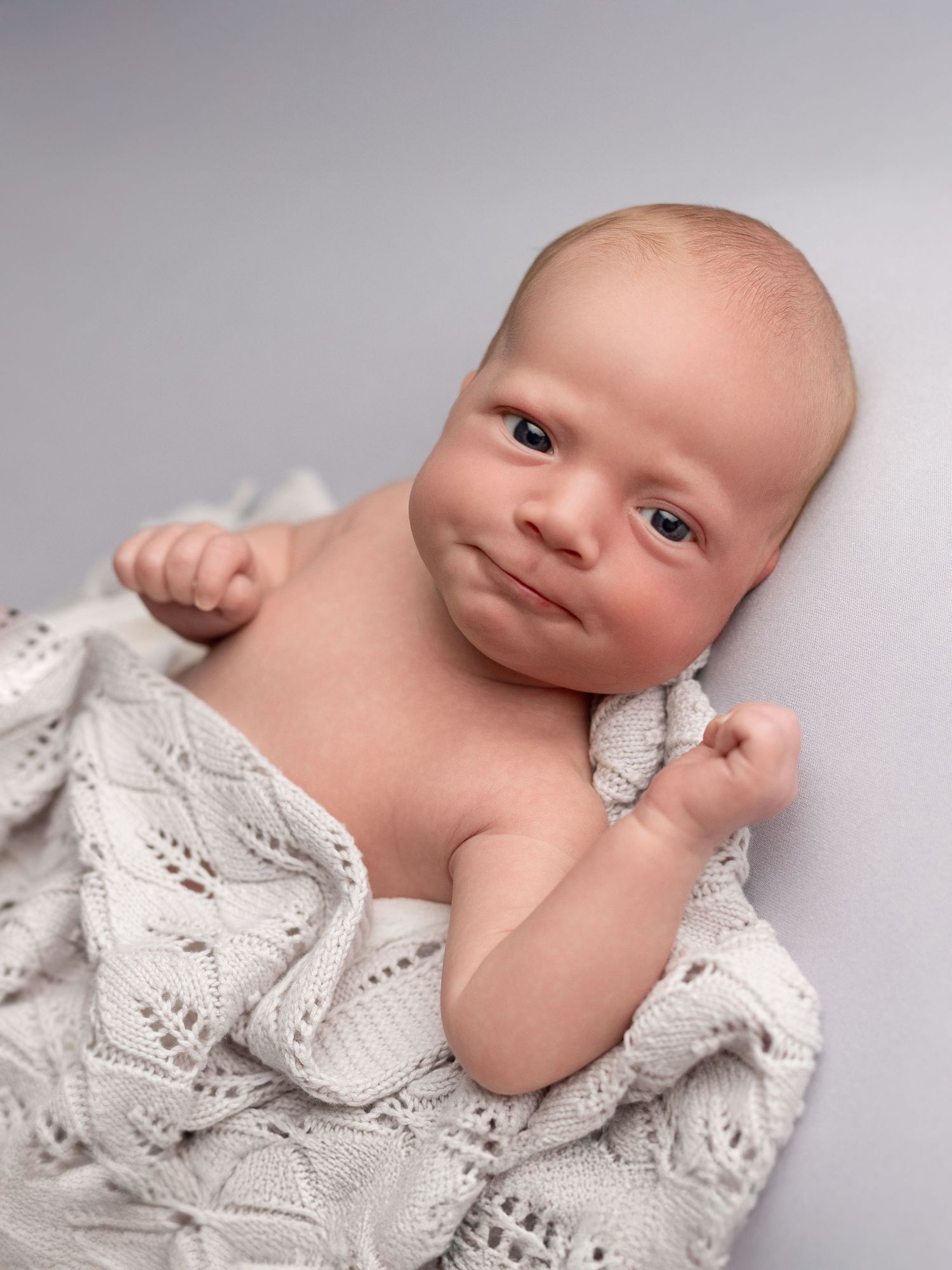 Newborn baby resting on white lace blanket in artistic portrait.