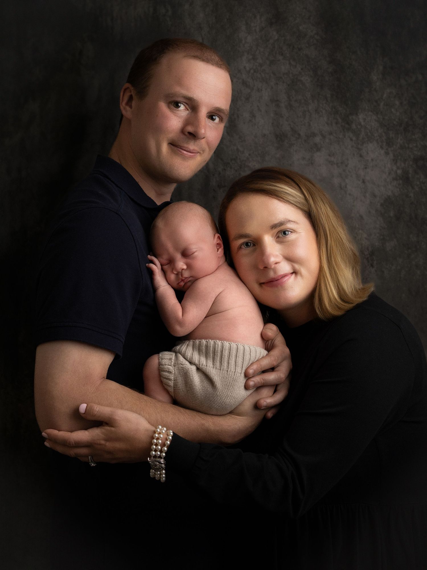 Family portrait series with newborn baby against dark dramatic background.