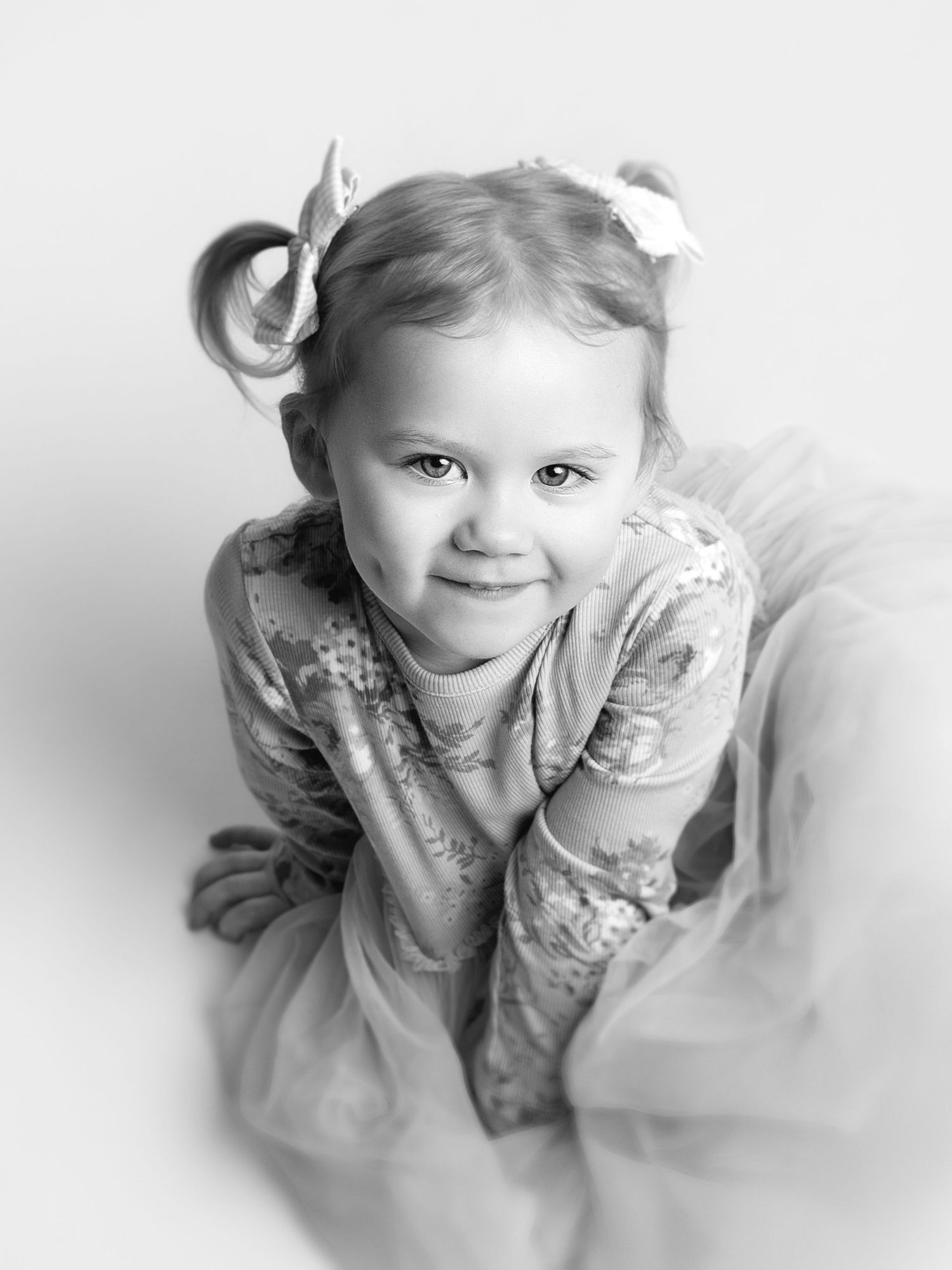 A black and white artistic photo series showing a young child in a floral dress making playful expressions.