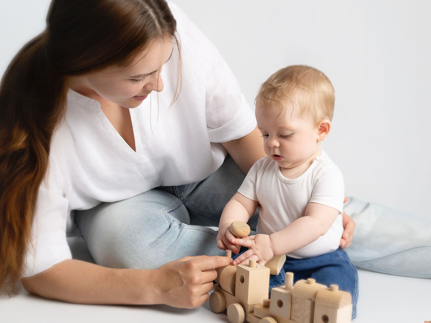 A young mother and baby play together with wooden building blocks on a white background.