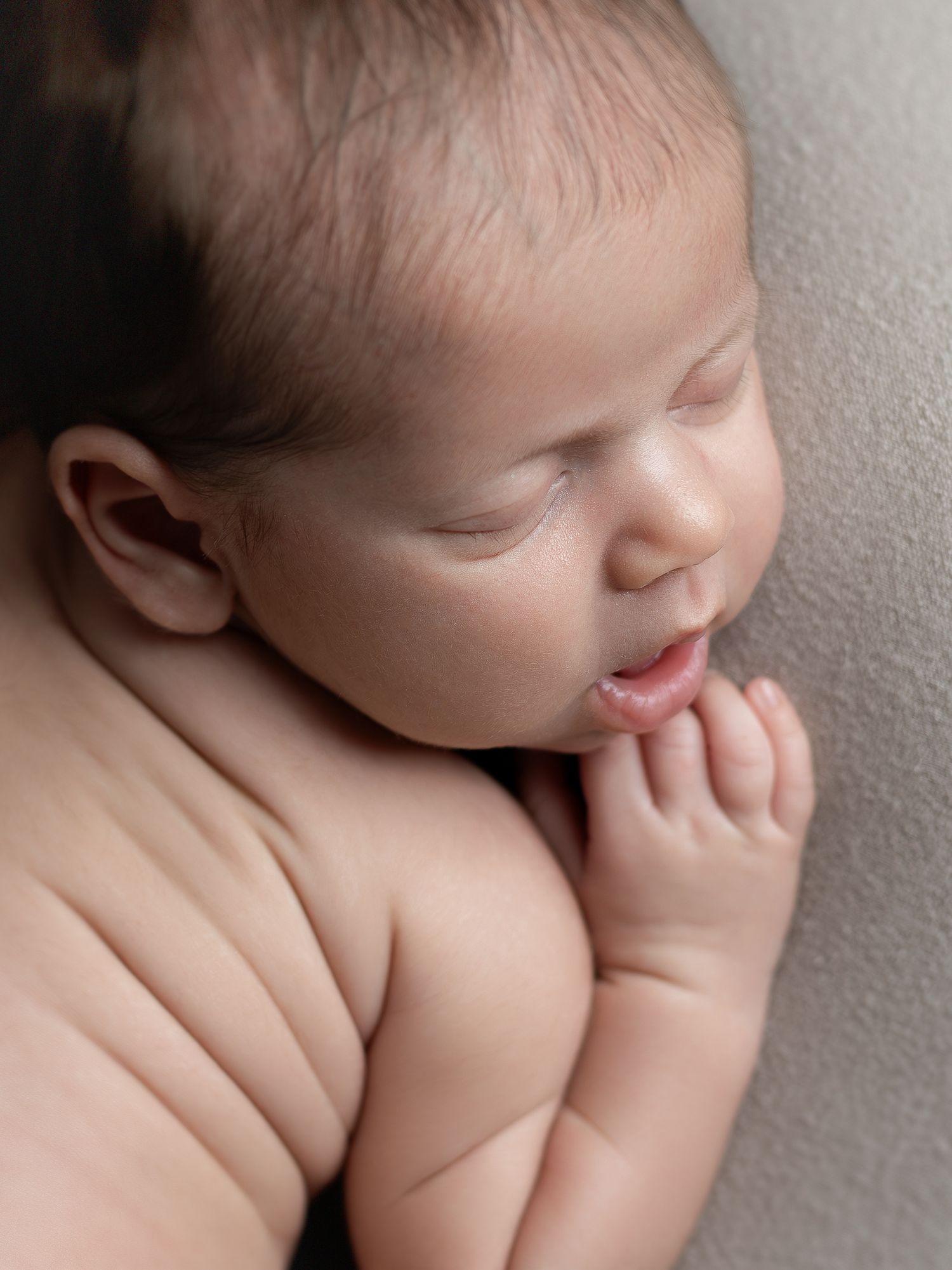 Peaceful sleeping newborn baby with tiny hands tucked under chin, soft skin glowing in gentle studio light.
