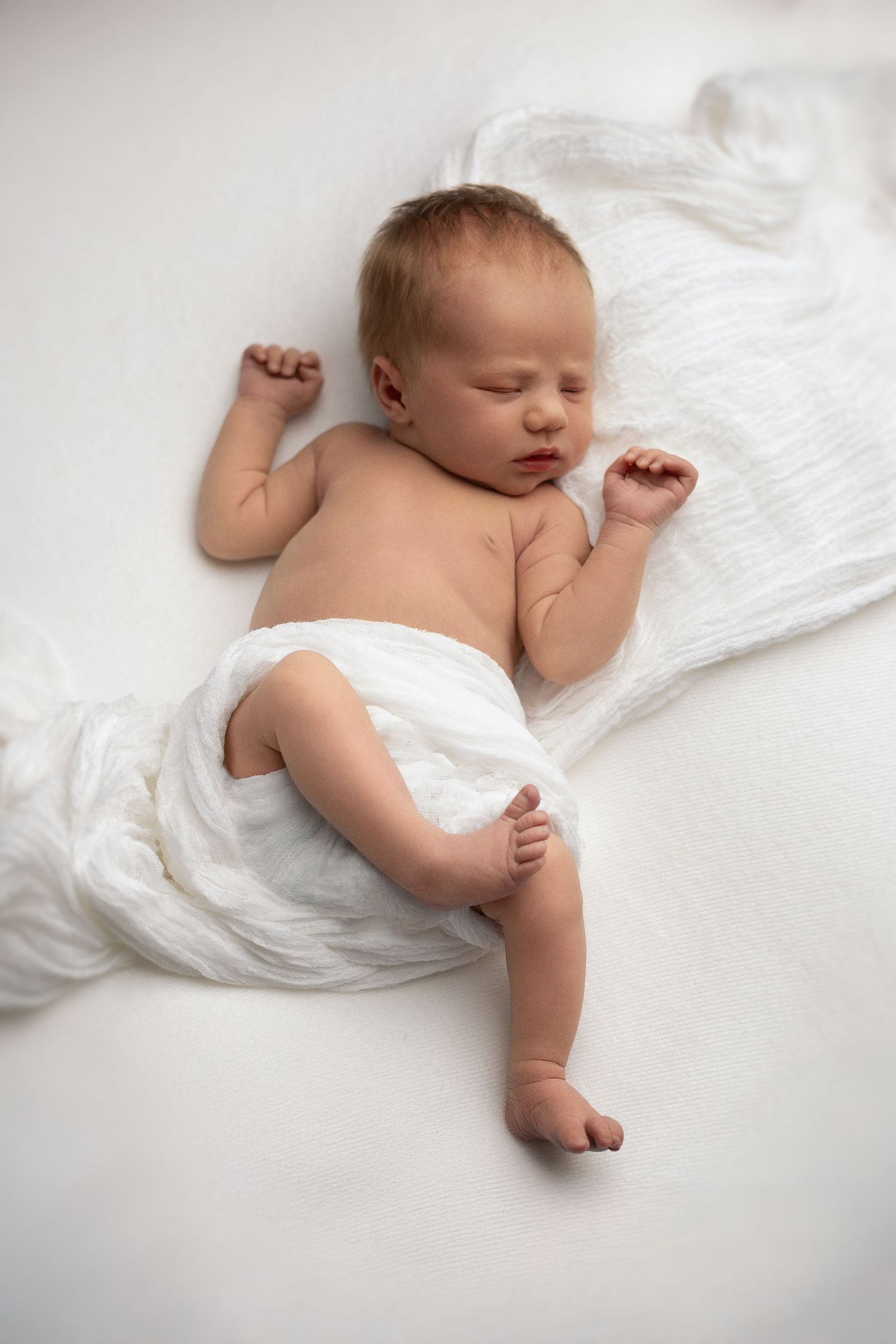 Sleeping newborn baby wrapped in white blanket on light background.