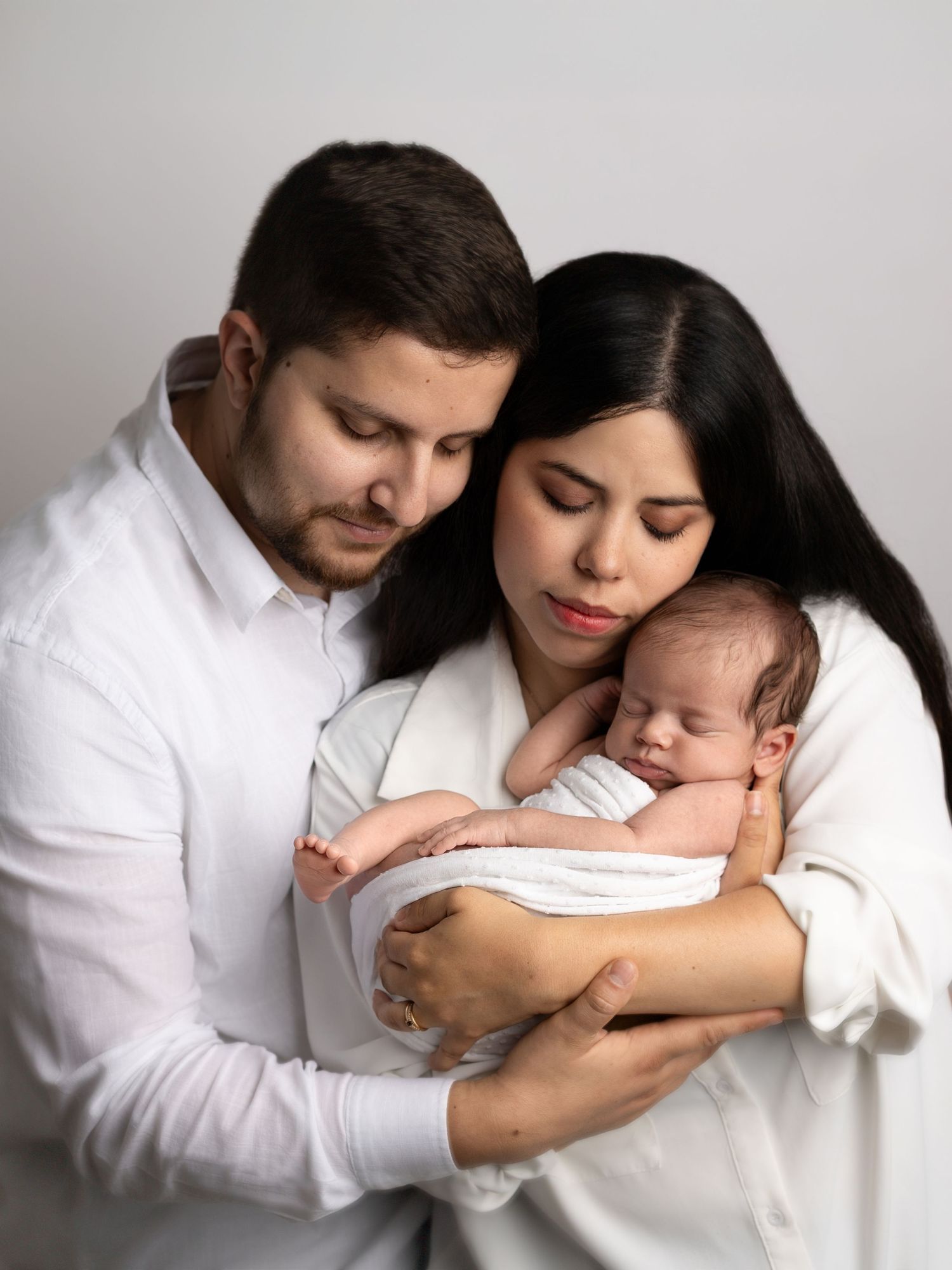 Tender family moment with sleeping newborn in professional studio setting.