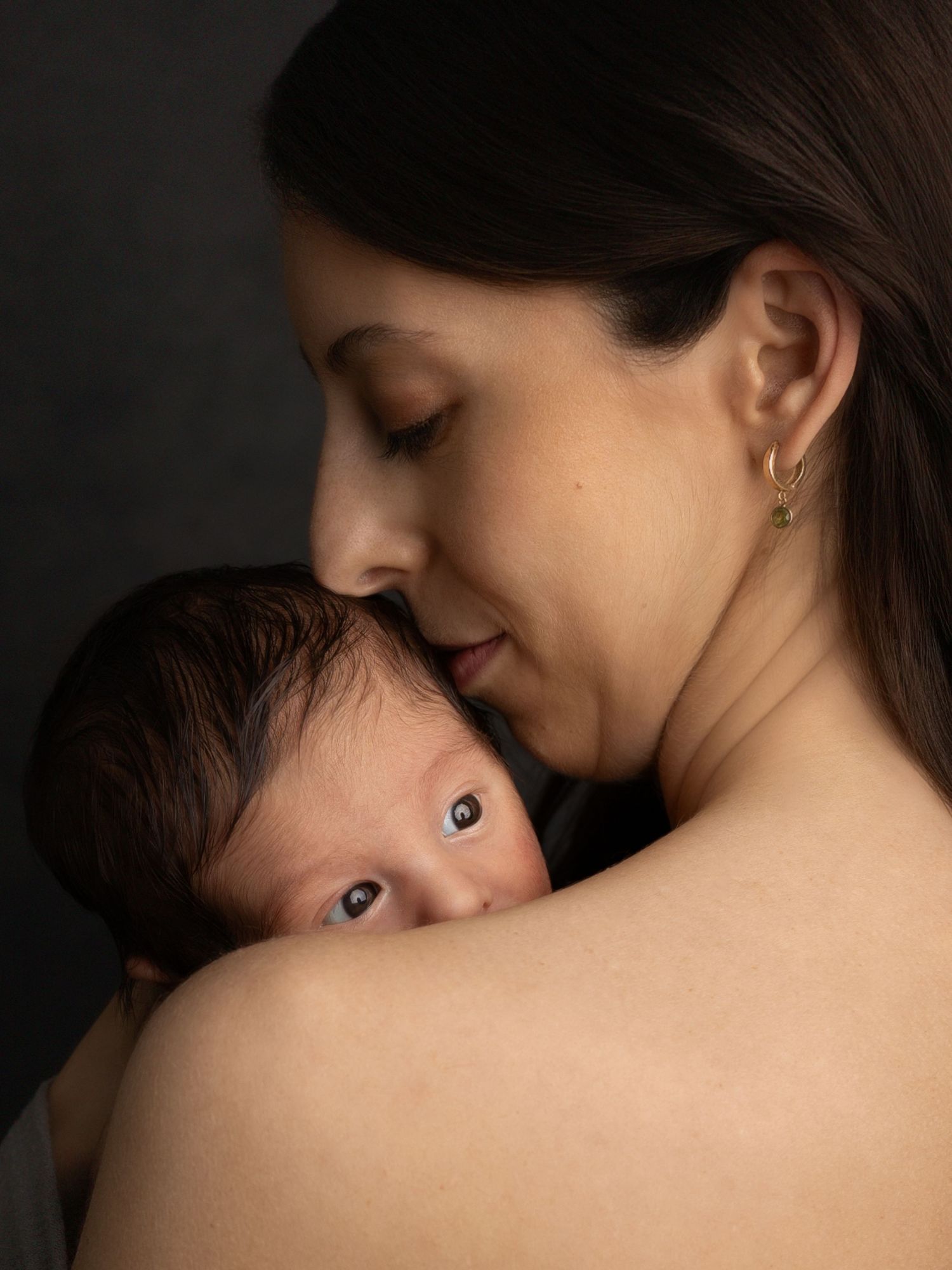 Intimate close-up portrait showing tender maternal moment against dark background