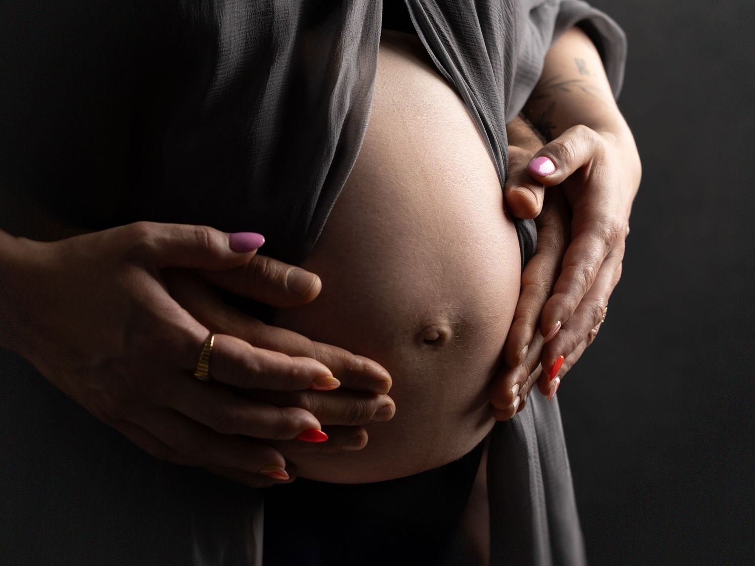Artistic close-up of hands gently resting on pregnant belly in dark setting.