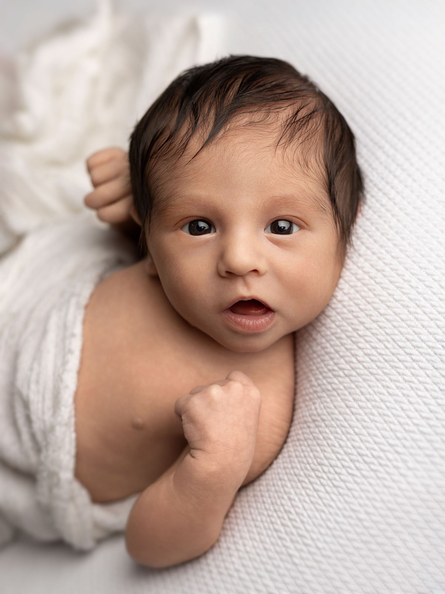 A newborn baby lying on white bedding is captured in a series of expressive close-up portraits.