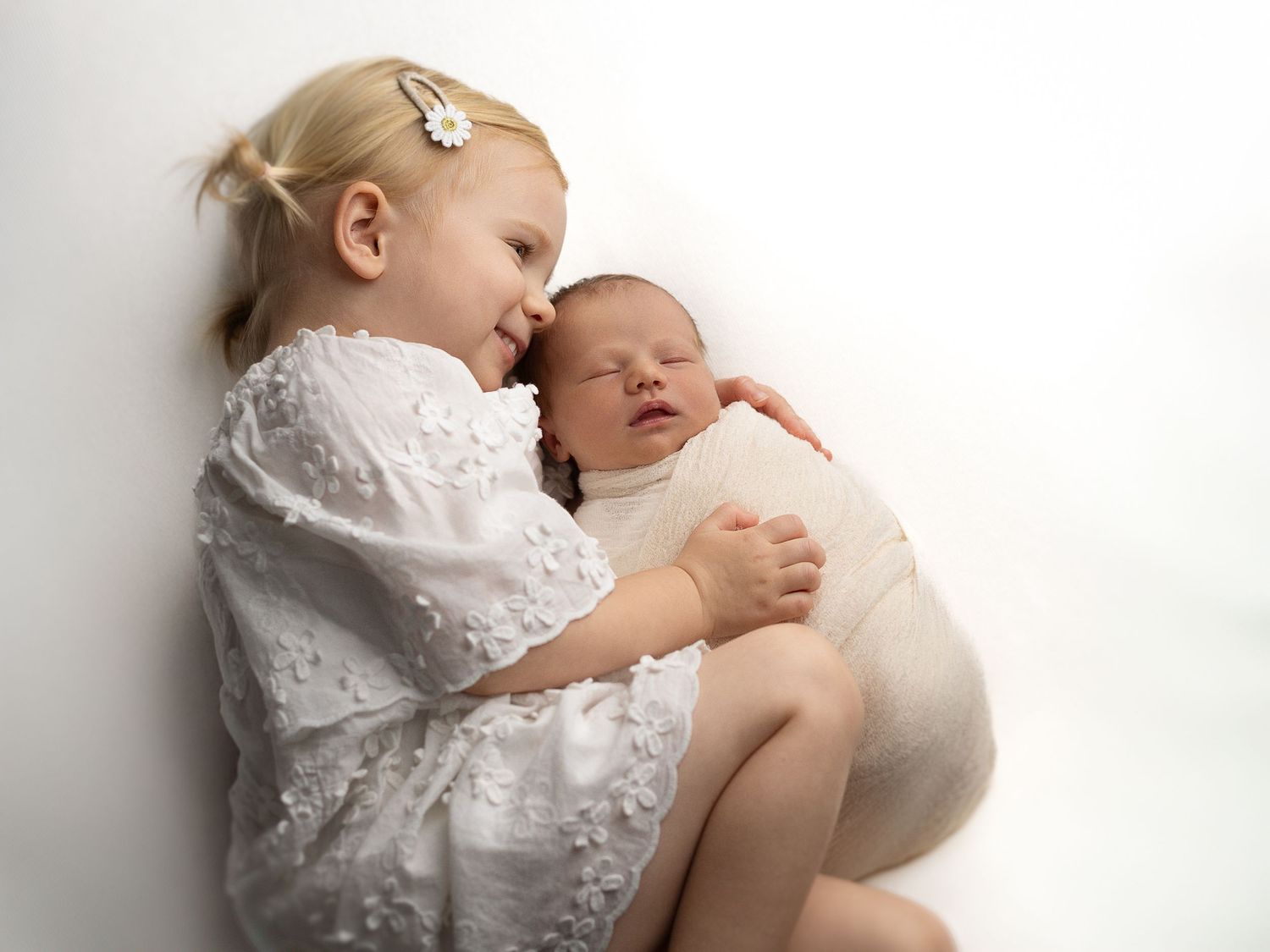 Baby in white lace outfit resting peacefully during newborn photo session.