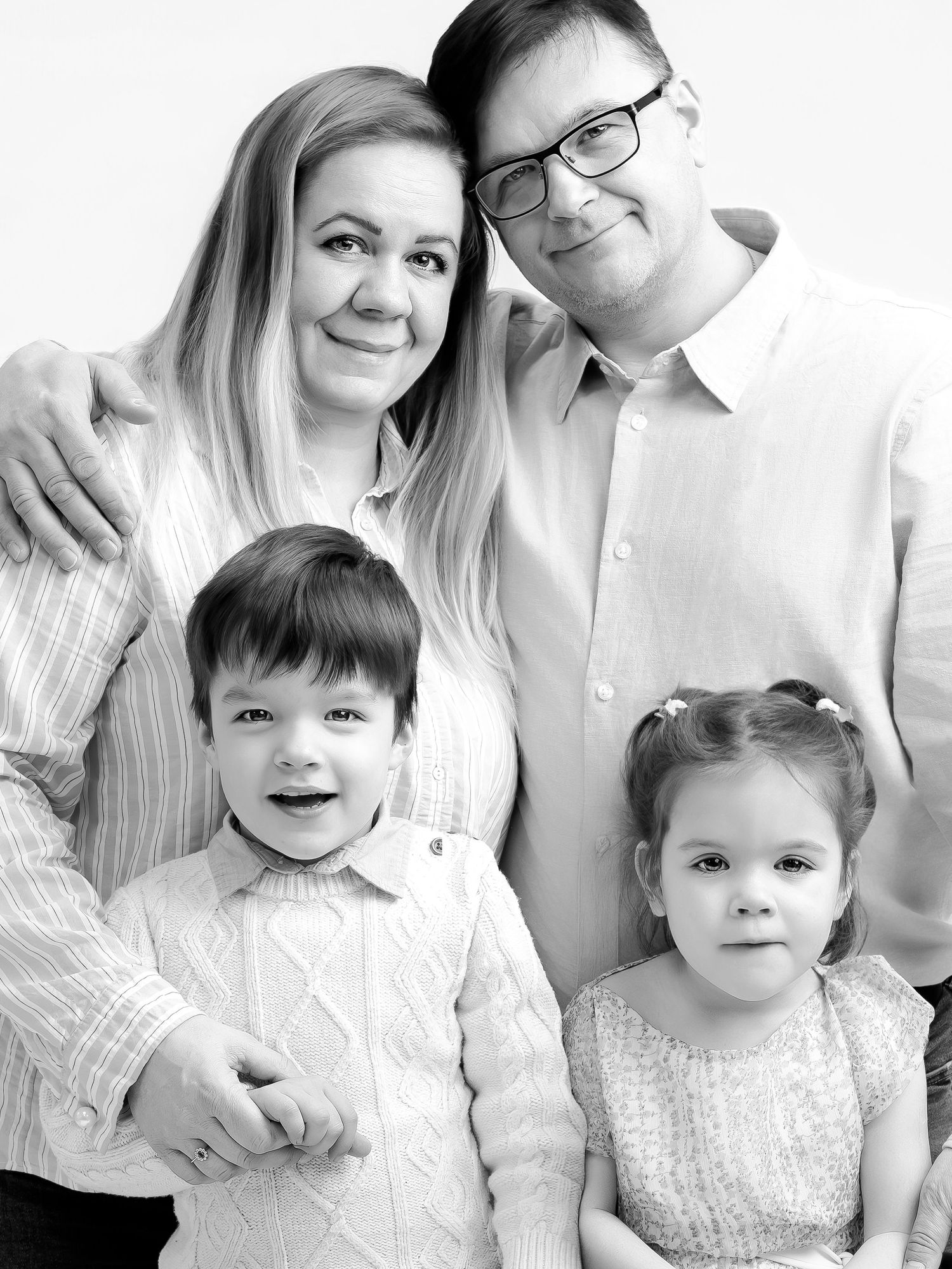 Black and white family portrait of two parents with young son and daughter posing together in a studio setting.