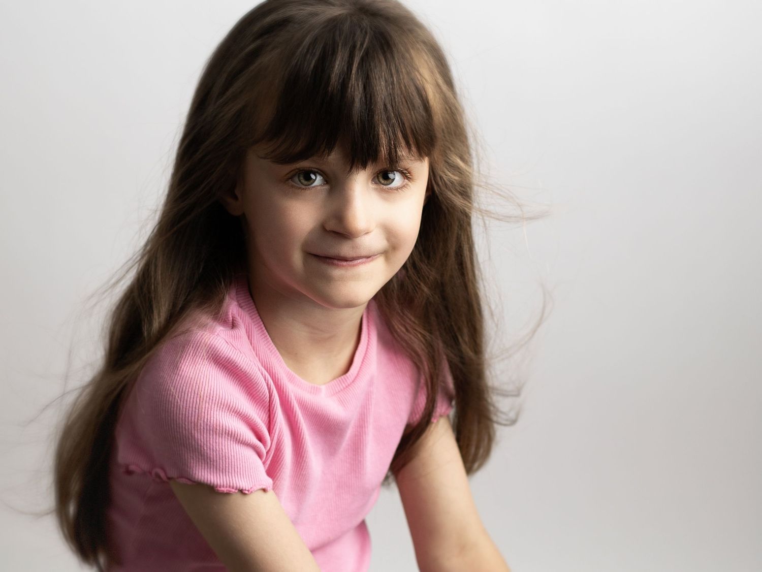 Portrait of child in pink shirt smiling against white background.