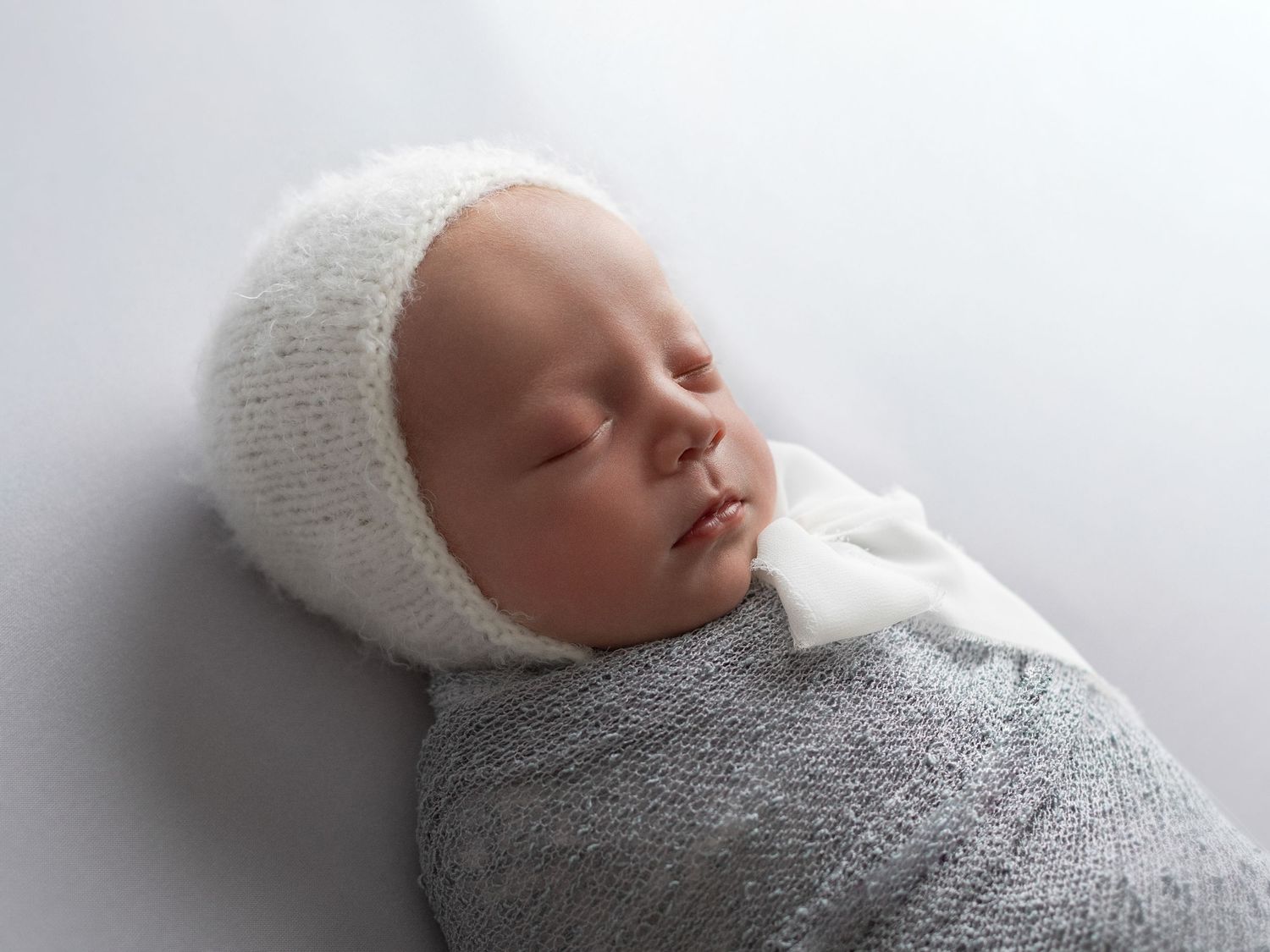 Peaceful newborn baby wrapped in gray and white knit blankets in various sleeping poses.