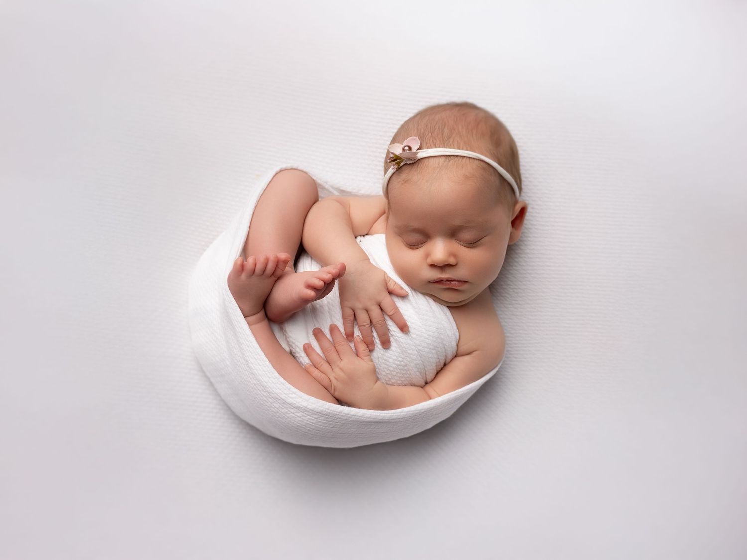 Artistic newborn photography series showing baby cradled in white fabric against light background.