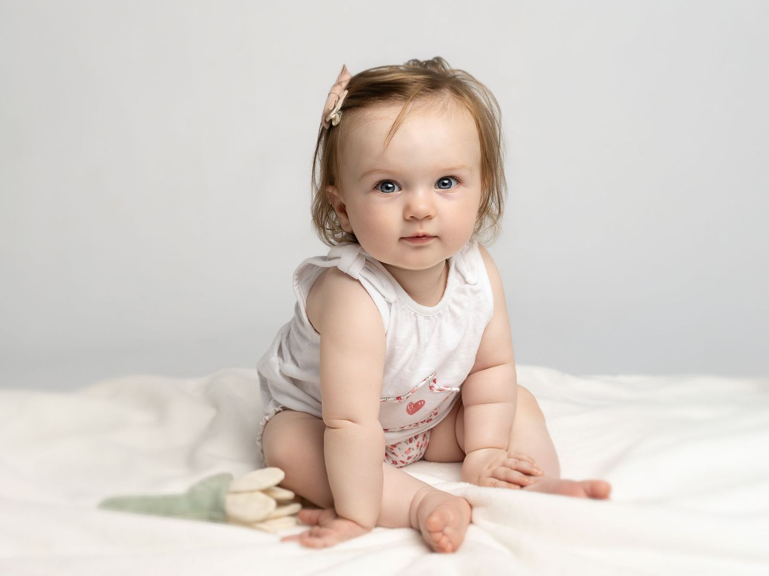Adorable baby girl in white romper sitting on a soft blanket with a tulip, studio portrait photography.