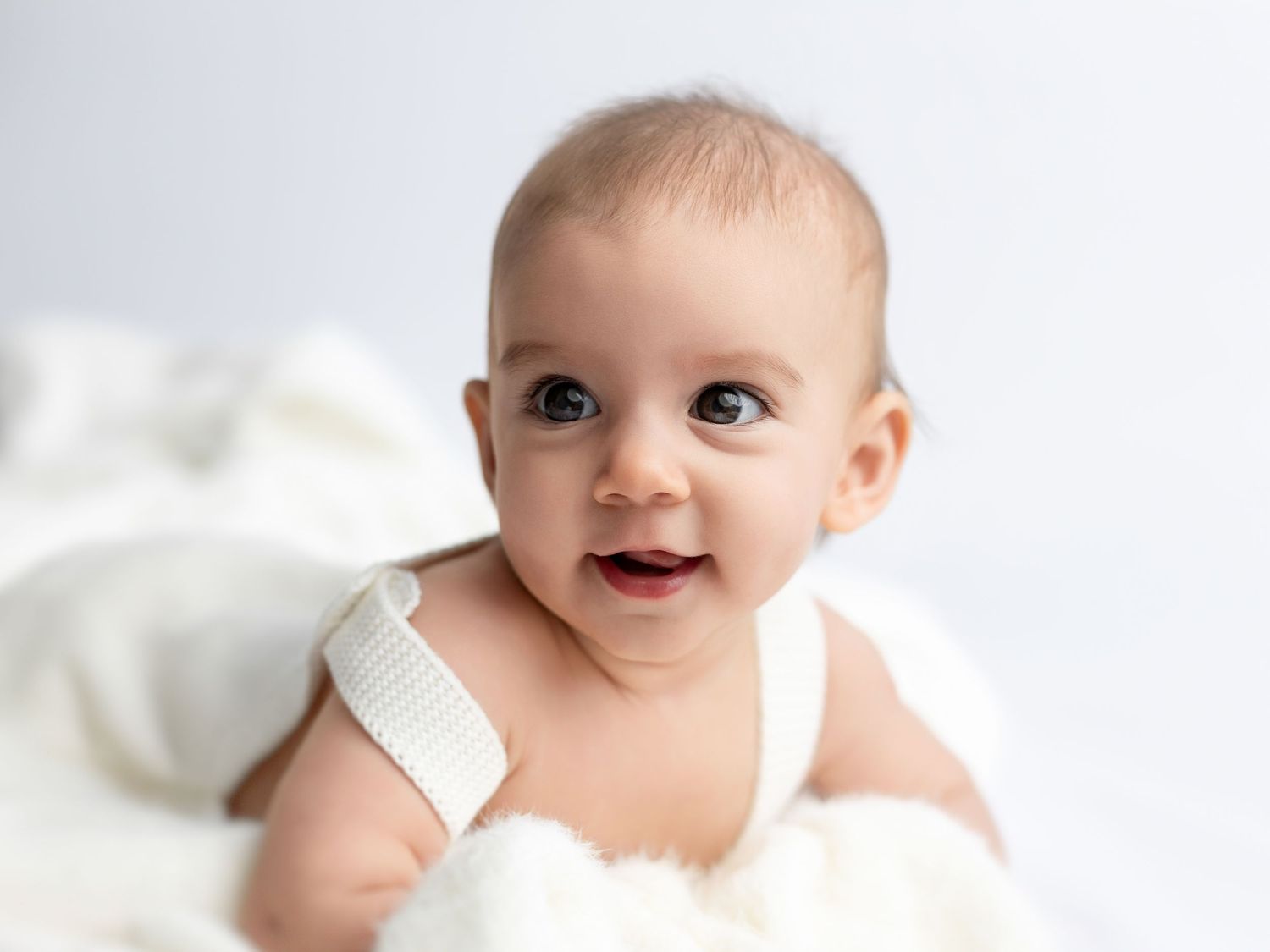 Baby in white outfit lying on light background showing playful expressions.